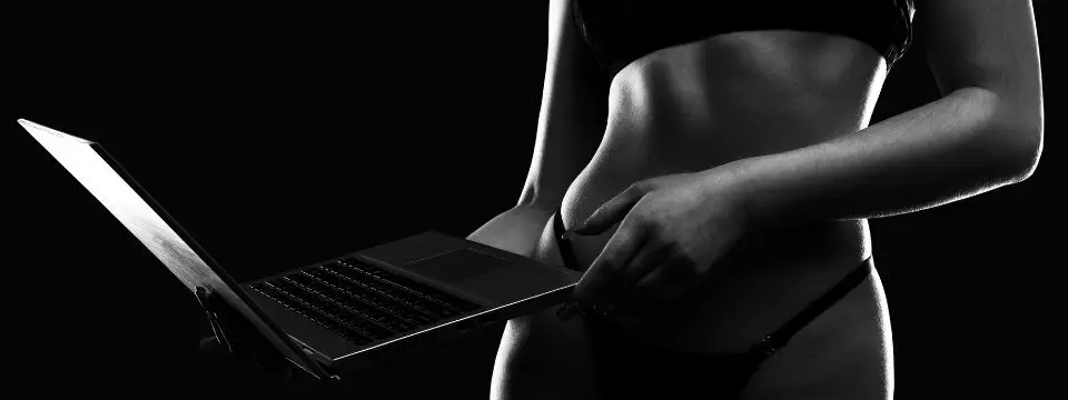 Black and white editorial image of a person holding a laptop against a dark background, representing online adult business, digital compliance, and content publishing.
